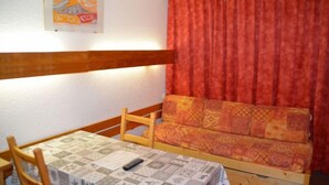A room with a wooden bench, a table with a patterned tablecloth, and a red curtain.