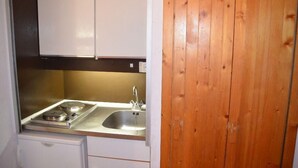 A compact kitchen with a stove, sink, and white cabinets.