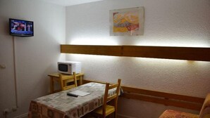 A small room with a bed, a table with a blanket, a TV, and a painting on the wall.