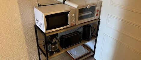 Une petite cuisine équipée d’un four à micro-ondes, d’un grille-pain, d’une machine à café et d’un petit four, le tout posé sur un support en métal noir.