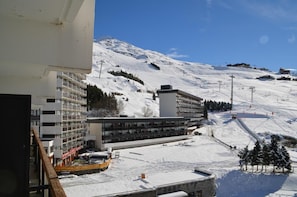 A modern hotel with a multi-story structure, a ski slope in the background, and a clear blue sky.