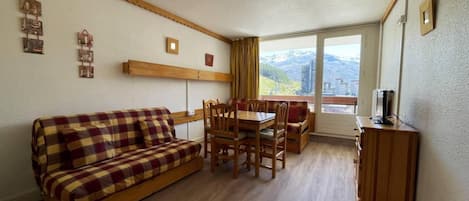 A furnished living room with a sofa, dining table, chairs, and a TV.