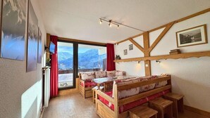 A cozy room with a wooden bed, a small table, and a bench. There is a window with a mountain view. - 10m from ski slopes, 7th floor, balcony, tv, 22m², Les Menuires (Les Menuires)