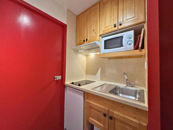 A compact kitchen with wooden cabinets, a microwave, a sink, and a dishwasher.