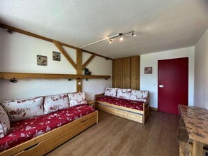 A room with two wooden beds with red bedding, a wooden ceiling with exposed beams, and a red door.
