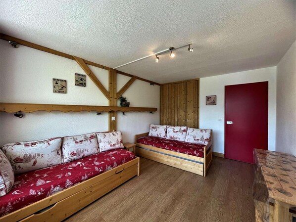 A room with two wooden beds with red bedding, a wooden ceiling with exposed beams, and a red door.