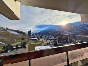 A view from a balcony overlooking a ski resort with buildings, a ski lift, and a mountain backdrop.
