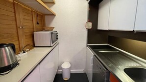 A compact kitchen with white cabinets, a microwave, a kettle, a sink, and a small trash bin. - 10m from ski slopes, 7th floor, balcony, tv, 36m², Les Menuires (Les Menuires)