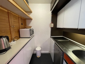A compact kitchen with a microwave, toaster, and stainless steel sink.