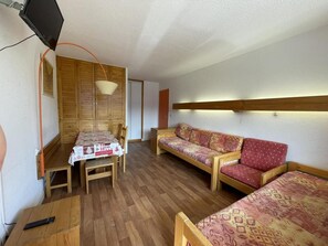 Een kamer met een houten tafel, een bank en een aan de muur bevestigde televisie.