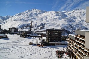 A snow-covered mountain with buildings in the foreground, including a multi-story hotel with balconies and a ski lift visible. - 10m from ski slopes, 7th floor, balcony, tv, 36m², Les Menuires (Les Menuires)