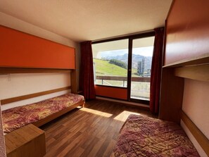 A room with two beds, a large window, and a view of a landscape.