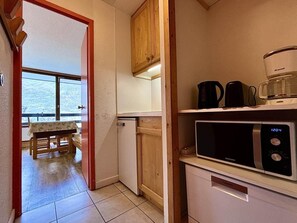 A compact kitchen with a microwave, coffee maker, and a small refrigerator. A wooden cabinet and a table with a view are also visible. - 10m from ski slopes, 8th floor, balcony, tv, 18m², Les Menuires (Les Menuires)