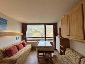 A cozy room with a sofa, a table, and a view of a valley through a large window. - 10m from ski slopes, 8th floor, balcony, tv, 18m², Les Menuires (Les Menuires)