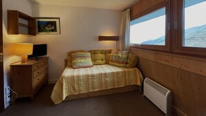 A bedroom with a bed, a dresser, a lamp, a radiator, and a window with a view. - 150m from shops, 7th floor, tv, ski locker, 13m², Les Menuires (Les Menuires)