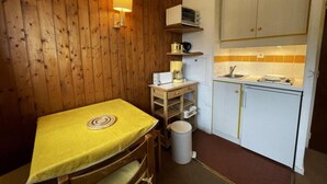 A compact kitchen with a wooden wall, a small dining table with a yellow tablecloth, a sink, a stove, and a microwave. - 150m from shops, 7th floor, tv, ski locker, 13m², Les Menuires (Les Menuires)
