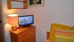 A room with a wooden dresser, a television displaying a news channel, a framed picture on the wall, and a yellow-striped pillow on the bed. - 150m from shops, 7th floor, tv, ski locker, 13m², Les Menuires (Les Menuires)