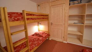 A bunk bed with a red patterned bedspread, a wooden wardrobe with a door, and a shelf unit with folded clothes. - 10m from ski slopes, 6th floor, balcony, tv, 55m², Les Menuires (Les Menuires)
