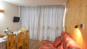 A room with a wooden dining table, chairs, a sofa, and a wall-mounted lamp. - 10m from ski slopes, 6th floor, balcony, tv, 55m², Les Menuires (Les Menuires)