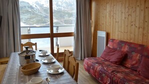 A cozy room with a wooden interior, a dining table set with dishes, a sofa, and a view of mountains through large windows. - 10m from ski slopes, 6th floor, balcony, tv, 55m², Les Menuires (Les Menuires)
