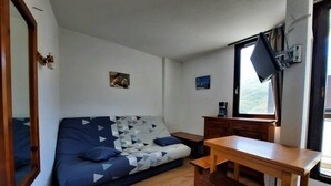 A compact room with a sofa, a wooden table, and a television. - 300m from resort center, 3rd floor, view mountain, balcony, tv, ski locker, 20m², Les Menuires (Les Menuires)