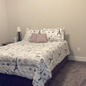 Cama com manta decorada com tema parisiense, luminária e tomada na parede.