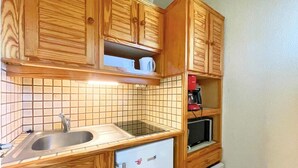 A compact kitchen with wooden cabinets, a sink, a microwave, and a small refrigerator. - 10m from ski slopes, Ground floor, balcony, tv, ski locker, 31m², Les Menuires (Les Menuires)