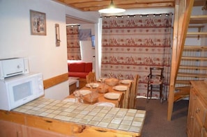 A dining area with a wooden table set for four, a red sofa, and a patterned curtain in the background. - 300m from shops, 2nd floor, view resort, balcony, tv, ski locker, 43m², Les Menuires (Les Menuires)