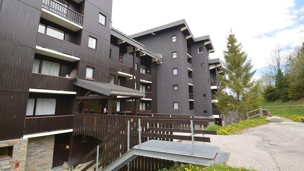 A multi-story building with balconies, a stone facade, and a paved area with a bench. - 10m from ski slopes, 4th floor, view resort, balcony, tv, ski locker, 60m², Les Menuires (Les Menuires)