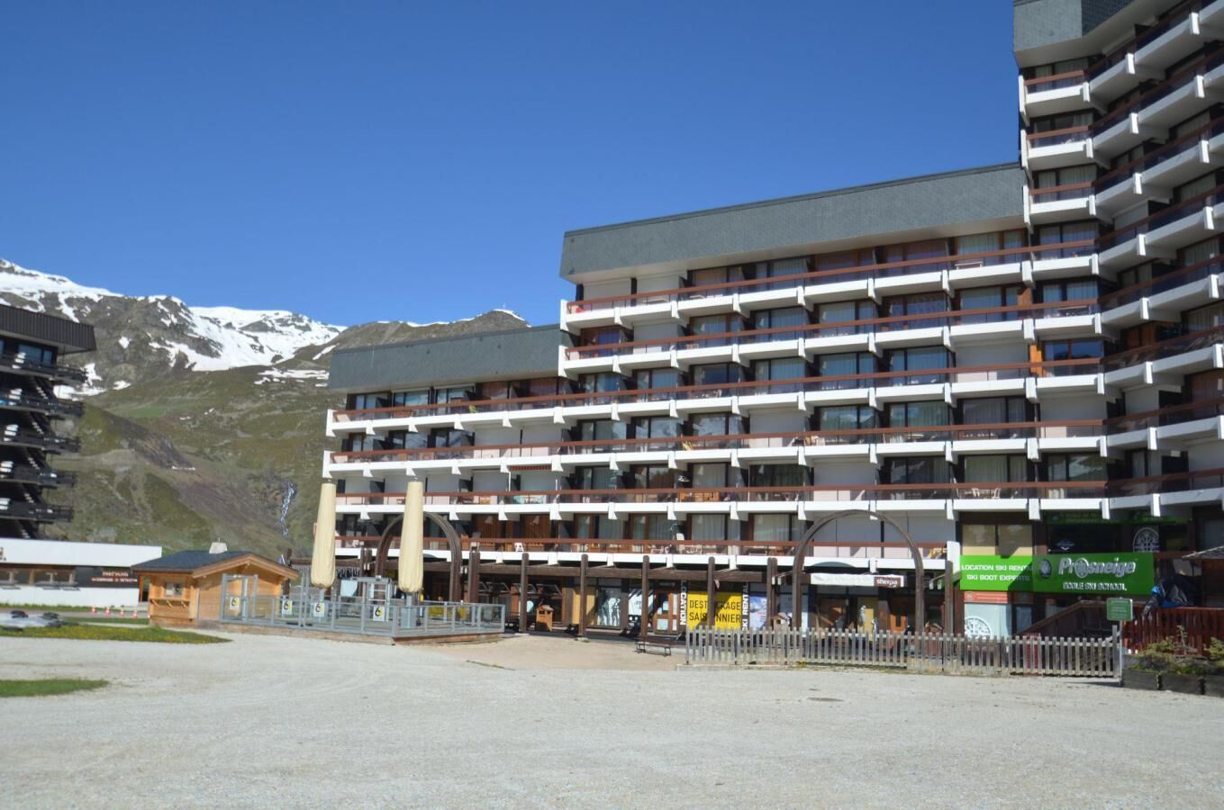 Et hotel med flere etager og balkoner, et skisportssted i baggrunden og en klar himmel.