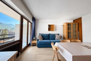 A modern room with a sofa, a dining table, and a cabinet. There is a large window providing a view of the outdoors.
