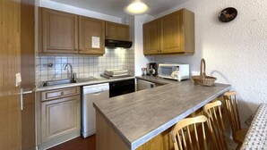 A compact kitchen with wooden cabinets, a built-in dishwasher, a microwave, and a large island with bar stools. - 200m from shops, 2nd floor, balcony, tv, ski locker, 44m², Les Menuires (Les Menuires)