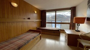 A room with a wooden bunk bed, a desk with a lamp, and a view of mountains through a large window. - 200m from shops, 2nd floor, balcony, tv, ski locker, 44m², Les Menuires (Les Menuires)