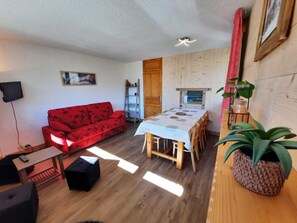 A living room with a red sofa, a dining table with chairs, a wooden floor, and a plant. - 10m from ski slopes, 10th floor, balcony, tv, ski locker, 48m², Les Menuires (Les Menuires)