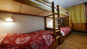A bunk bed room with a red patterned bedspread, wooden bunk beds, and a ladder. - 10m from ski slopes, 10th floor, balcony, tv, ski locker, 48m², Les Menuires (Les Menuires)