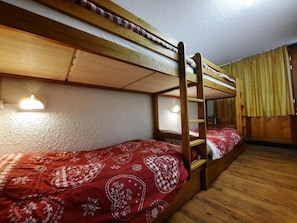 A bunk bed room with a ladder, wooden walls, and a window with curtains.