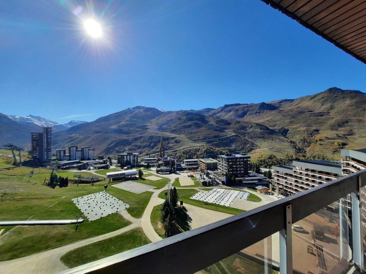 A high-rise building with a view of a mountainous landscape, a parking lot, and several buildings with flat roofs.
