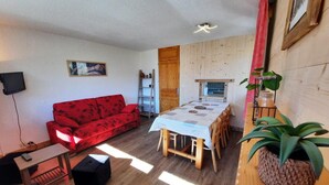 A cozy living room with a red sofa, a dining table, and a wooden floor. - 10m from ski slopes, 10th floor, balcony, tv, ski locker, 48m², Les Menuires (Les Menuires)