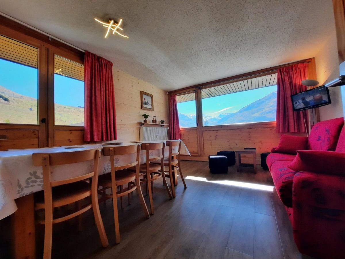 A room with a dining table, chairs, a red sofa, and a television.