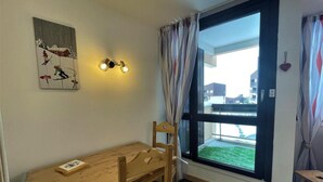 Una stanza con un tavolo e sedie in legno, un quadro appeso al muro, una finestra con tende e vista sugli edifici esterni.