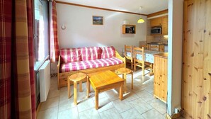 A cozy living room with a plaid sofa, wooden furniture, and a kitchen area with wooden cabinets and a microwave. - 150m from shops, 3rd floor, view ski slopes, balcony, tv, ski locker, 26m², Les Menuires (Les Menuires)