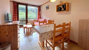 A cozy room with a wooden desk, a bed with a pink blanket, a small table, and a TV on the desk. - 150m from shops, 3rd floor, view ski slopes, balcony, tv, ski locker, 26m², Les Menuires (Les Menuires)