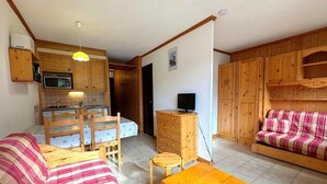 A cozy living room with a sofa, a wooden coffee table, and a television. There is a kitchen area with wooden cabinets and a microwave. - 150m from shops, 3rd floor, view ski slopes, balcony, tv, ski locker, 26m², Les Menuires (Les Menuires)