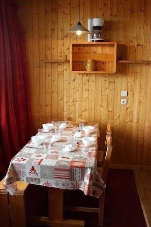 A wooden-paneled room with a table set for dining, a coffee machine, and a shelf with a mug.