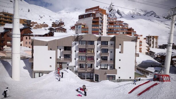 Une station de ski dotée d’un bâtiment moderne, avec de nombreux balcons, et un télésiège visible en arrière-plan.