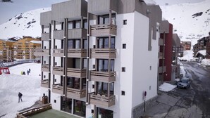 Un immeuble à plusieurs étages doté de balcons, un télésiège en arrière-plan et une montagne enneigée.