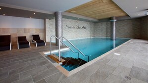 Piscina interna com teto de madeira, paredes revestidas de azulejos e área ao redor da piscina com cadeiras.
