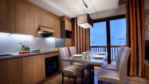 A modern kitchen with wooden cabinets, a dining table set for four, and a view of a snowy landscape through large windows. - Wifi, ski-in/ski-out & foot of the slopes, fitness, swimming pool, sauna, hammam, balcony, tv (Les Arcs)