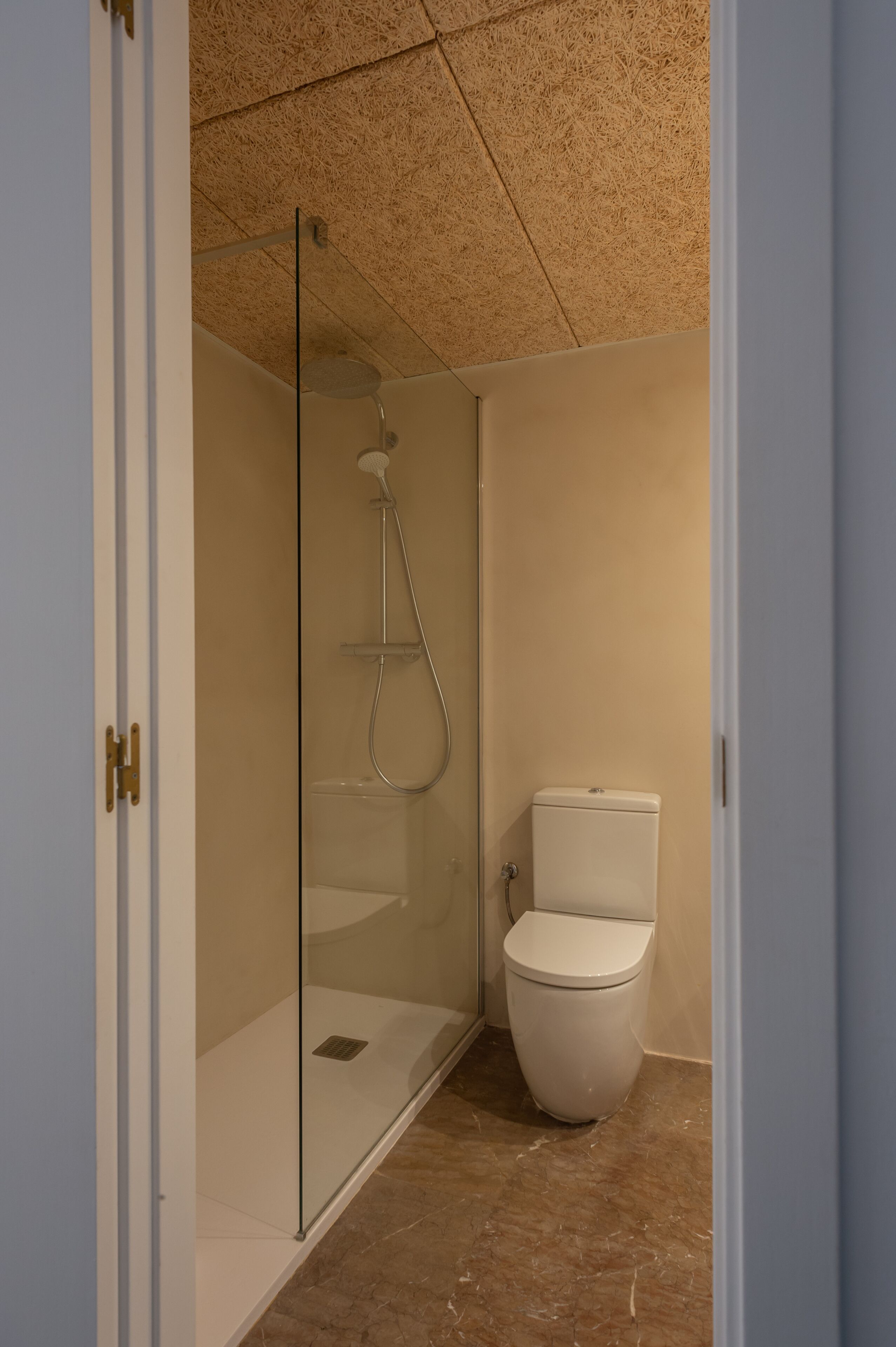 A bathroom with a glass-enclosed shower, a toilet, and a marble floor.