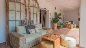 A cozy living room with a wicker sofa, a wooden coffee table, and a large potted plant. - Hostal Es Niu de Tamariu (Palafrugell)